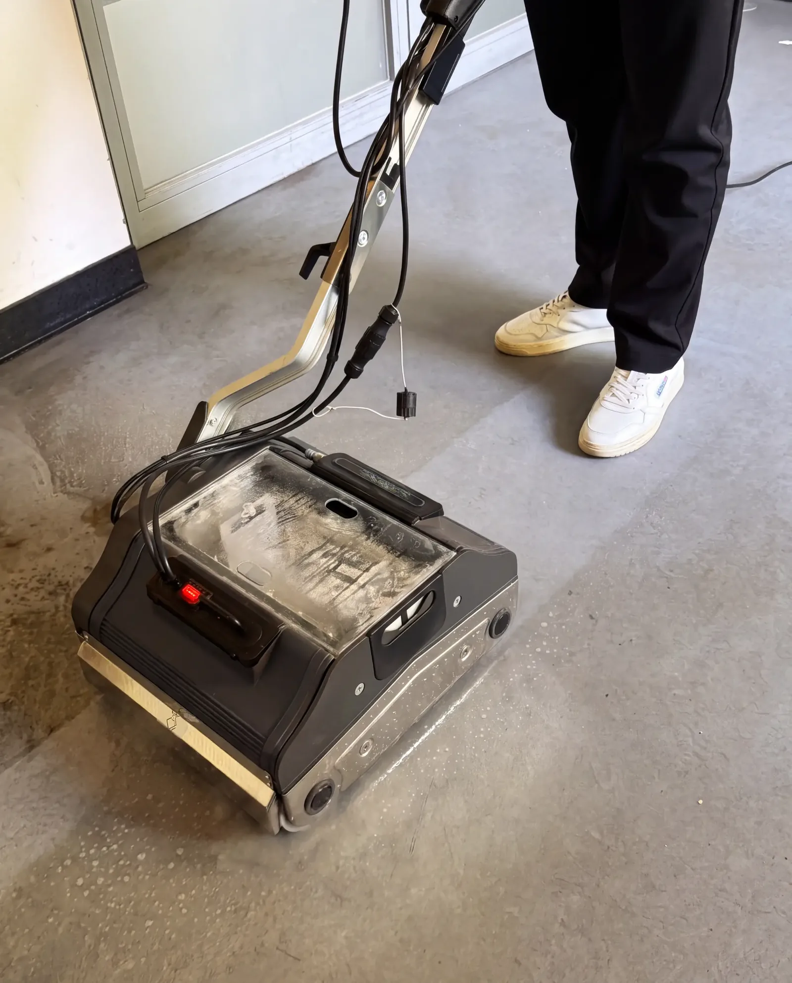 Eine Person führt die Terra über einen Betonboden, neben der Maschine der frisch gereinigte Streifen